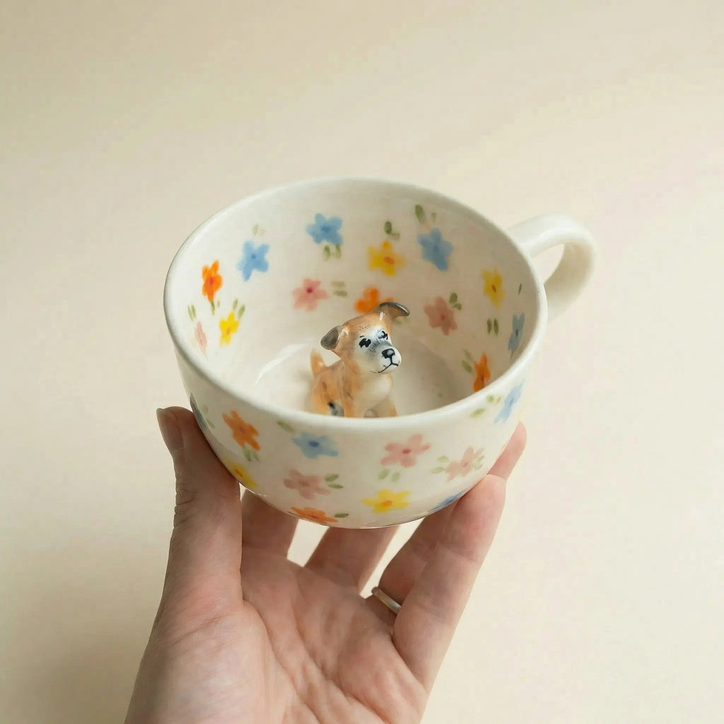 Hand holding floral mug with dog figurine