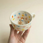 Hand holding floral mug with dog figurine